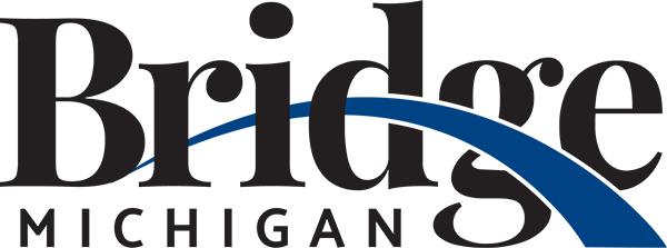 The logo of Bridge Michigan features the word 'Bridge' in bold black letters, with 'Michigan' in smaller black text below. A blue arc connects the two words, symbolizing a bridge. The design emphasizes clarity and is simple in style.