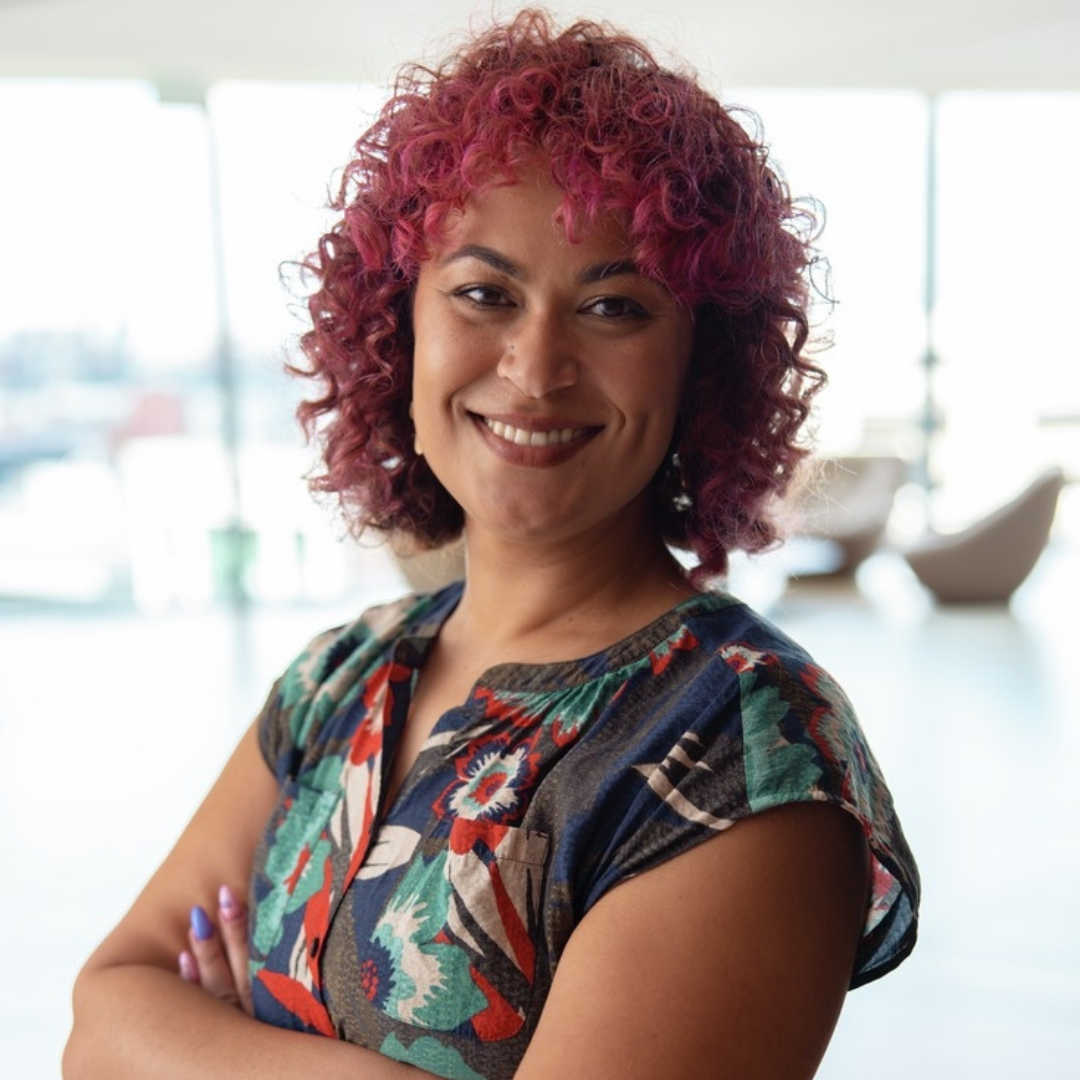 Andrea Washington smiling with her arms crossed, wearing a colorful floral-patterned shirt. The background features a bright, modern interior with large windows and soft seating.